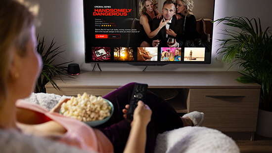 person holding a bowl of popcorn and remote control looking at a tv