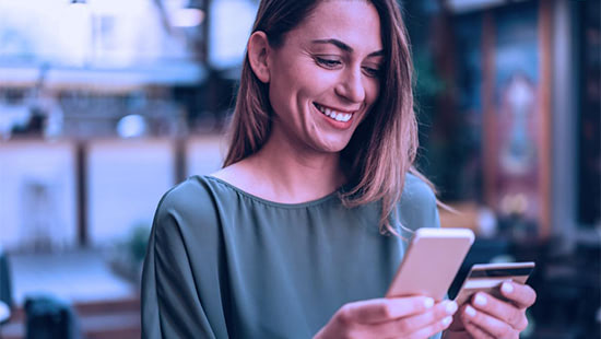 Young smiling woman holding a mobile phone in one hand and a credit card in another