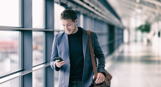 Business man walking through airport using his mobile