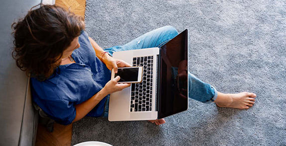 Woman sitting on the floor texting with a laptop on lap