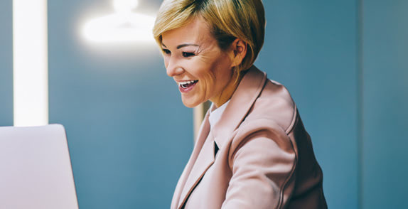 Woman in an empty meeting room laughing looking at laptop screen