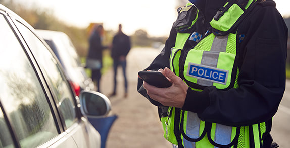 Police officer next to parked car looking down at phone