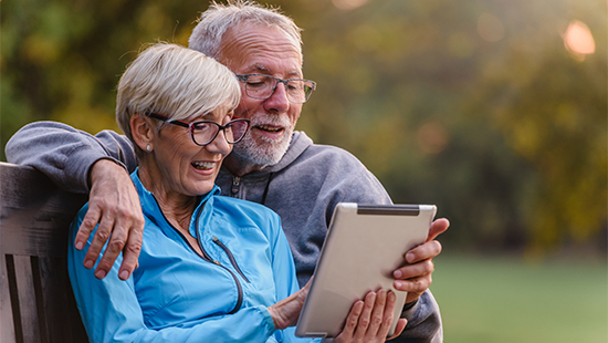 Couple sat on a park bench looking at a tablet together