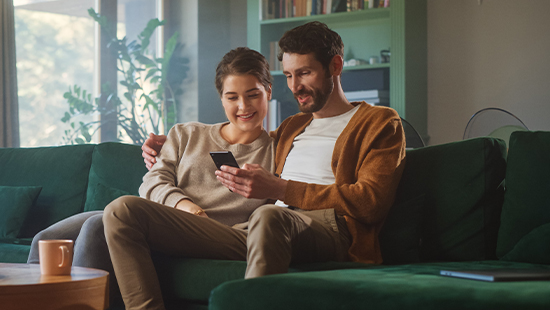 Couple sat on a sofa looking at a phone together