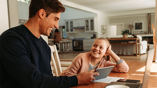 Father and daughter sat in kitchen looking at a tablet