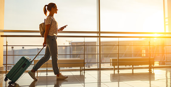 Woman walking through an airport using her mobile and pulling a bag