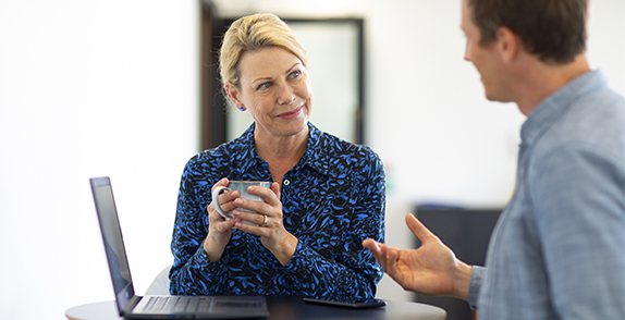 Woman holding a mug talking to a man using a computer