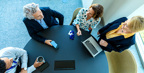 Group of people sat around a meeting table using mobile phones and laptops