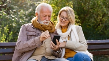 Two people sitting on a bench looking at smartphone