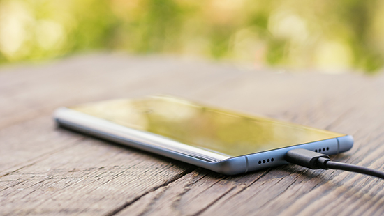 Smartphone plugged in to charging cable, on a wooden table with trees in background