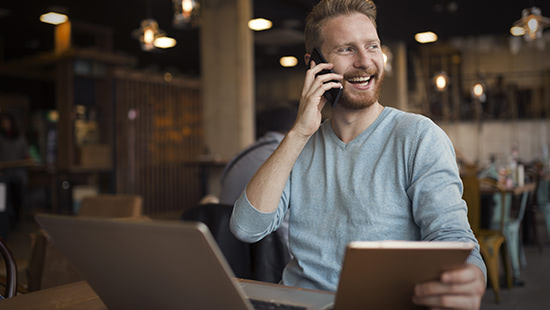 person sitting in front of a laptop holding a phone to their ear