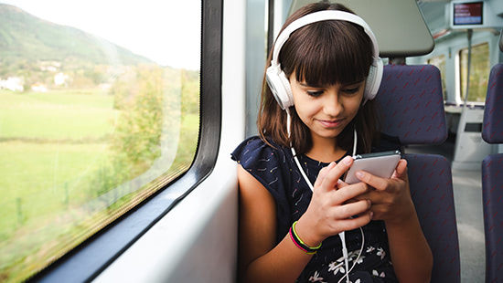child on a train wearing headphones and holding a phone