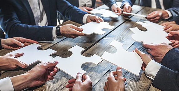 Colleagues sat around a meeting table holding various puzzle pieces