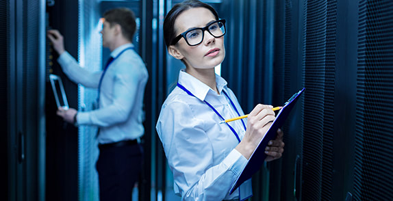 Woman holding a clipboard looking at servers and man holding tablet looking at system