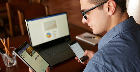 Man sat at a table looking at a tablet, phone and computer