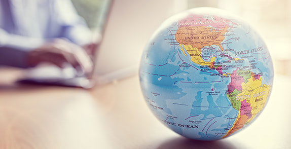 Globe on a table next to person working on a laptop