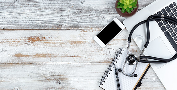 Stethoscope, laptop, phone, notepad and succulent on a wooden table