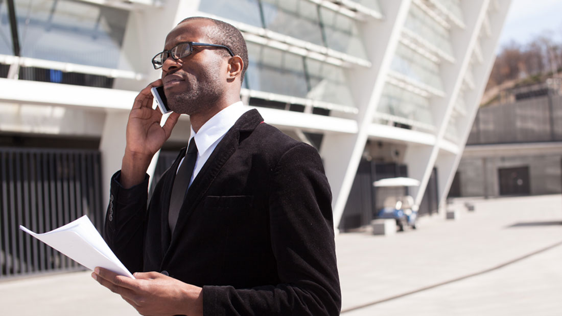 Businessman holding mobile phone in front of office building