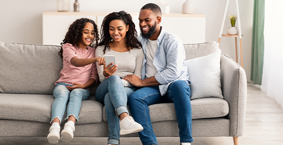 three people sat on a sofa looking at a phone