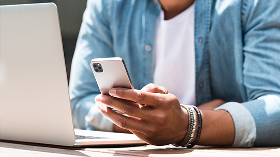 person holding their phone and sitting with a laptop