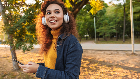 person wearing headphones holding their phone under a tree