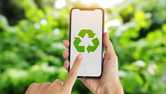 person holding their phone with a recycle sign on it in front of greenery