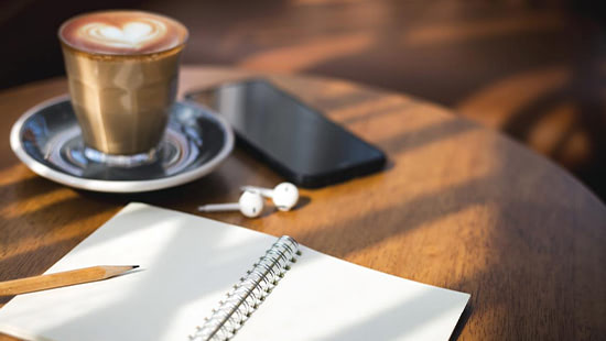 coffee, earbuds, phone and notebook on a table