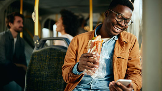 person on a bus eating a sandwich and laughing at their phone