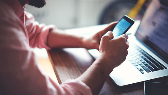 person holding phone in front of a laptop