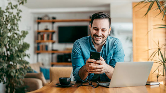 Man holding mobile phone in front of laptop