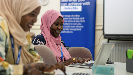 Black women wearing headscarves sitting at tables on laptops